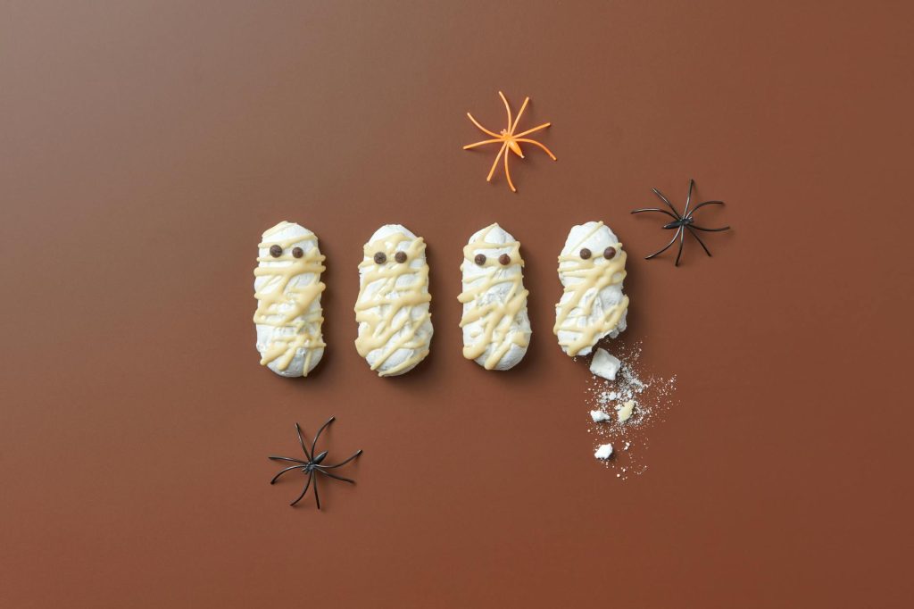 Halloween mummy cookies with icing and toy spiders on a brown background.