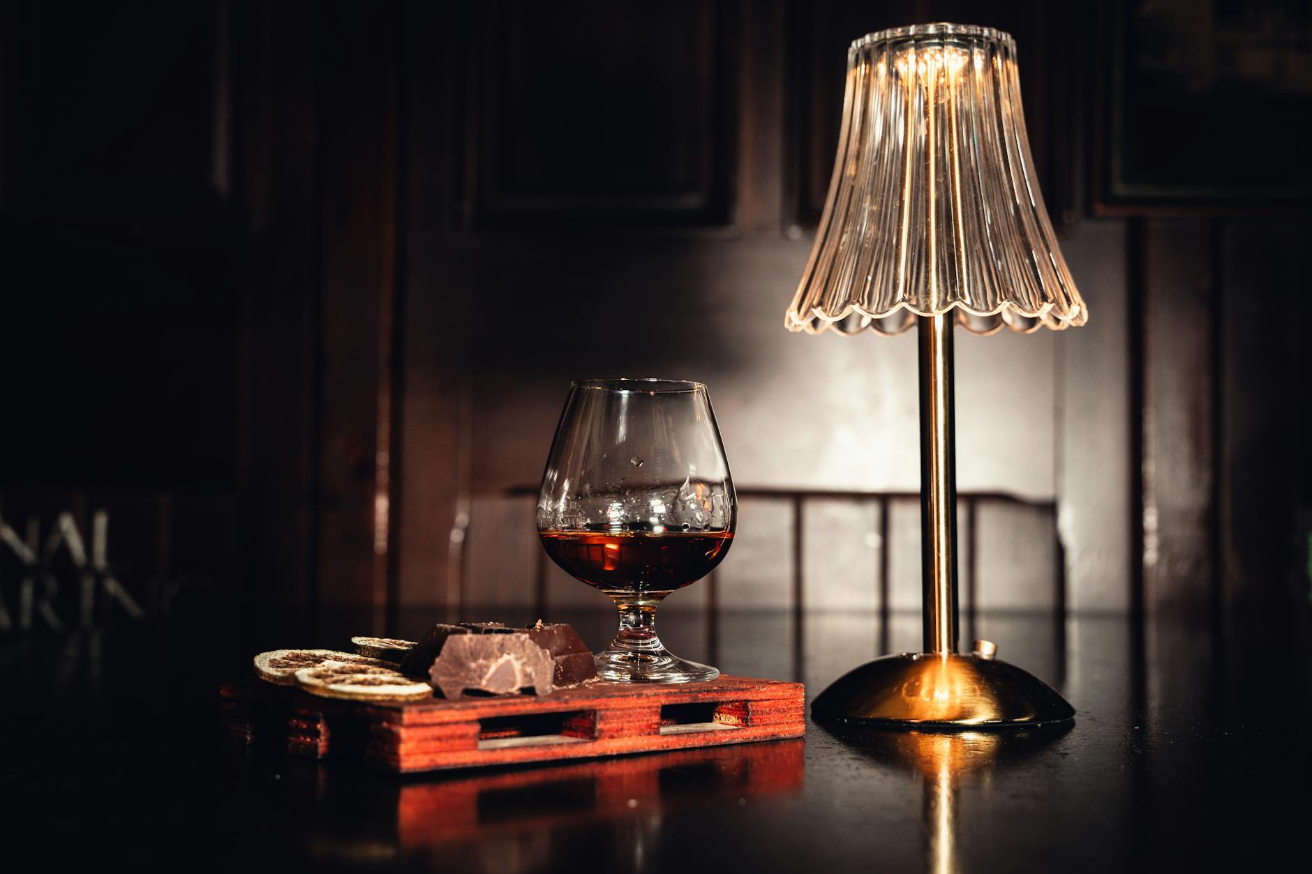 Chocolate Bars Evolution: Must-Have Timeline with Delicious Innovations A cozy and elegant bar scene featuring a glass of cognac and a warm lit lamp.