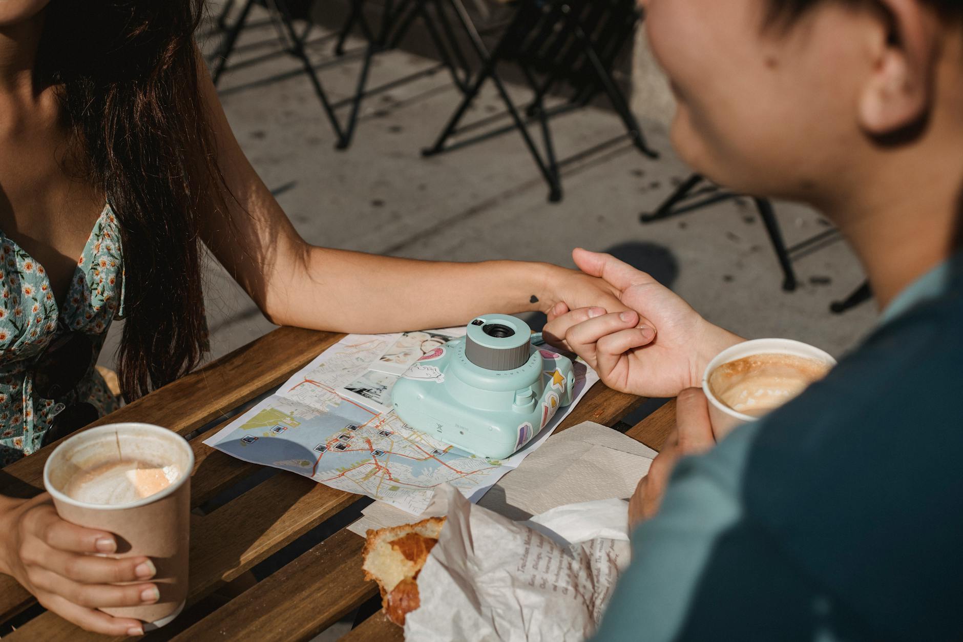 Cocoa Bean: Best Practices for an Effortless Journey Romantic couple enjoying coffee and pastries outdoors, holding hands with a map and camera on the table.